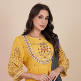 Portrait of a woman, Farah Rez, looking at the camera, wearing the embroidered MALIKA dress against a warm cream background.
