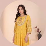 Circular portrait of Yasmine B. smiling, wearing the embroidered MALIKA dress against a warm cream background with dusty rose